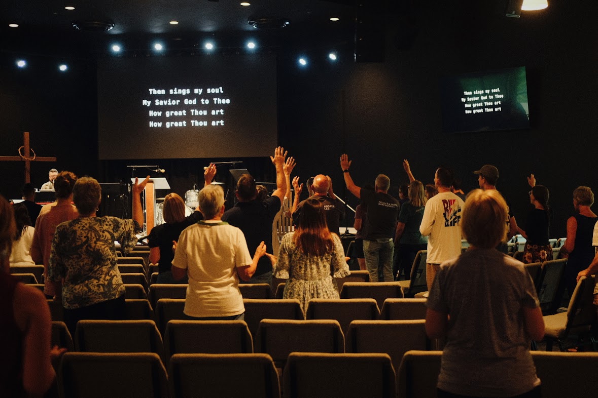 Liturgy People standing in a church, raising hands in worship, with hymn lyrics displayed on screens at the front.