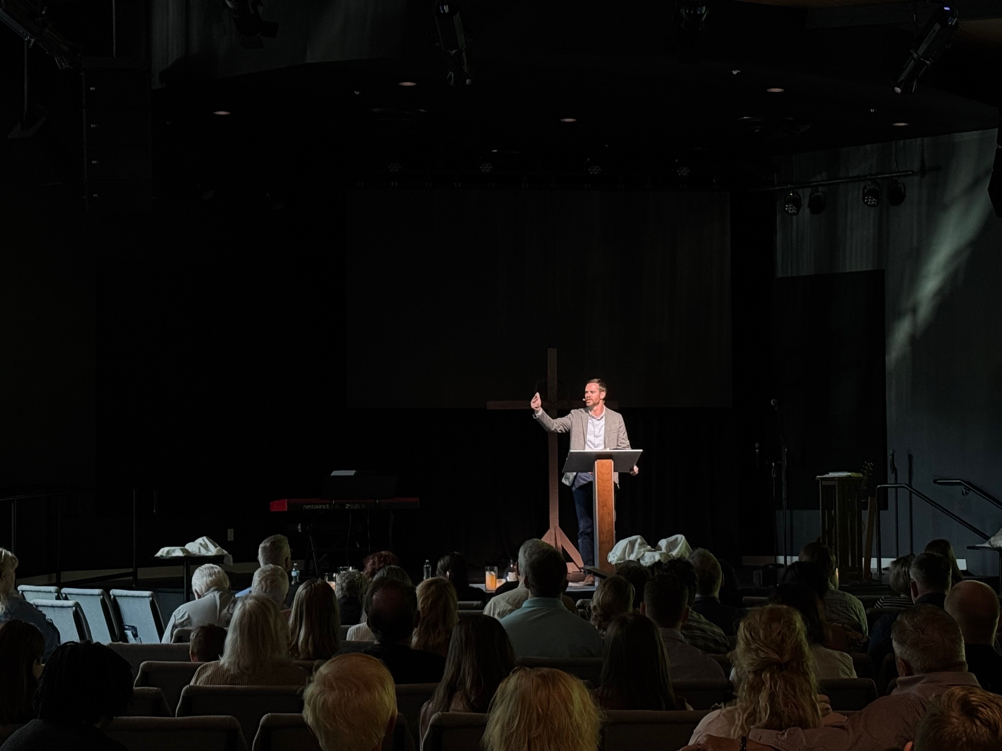 Preaching A man speaks at a podium to a seated audience in a dimly lit church or auditorium.