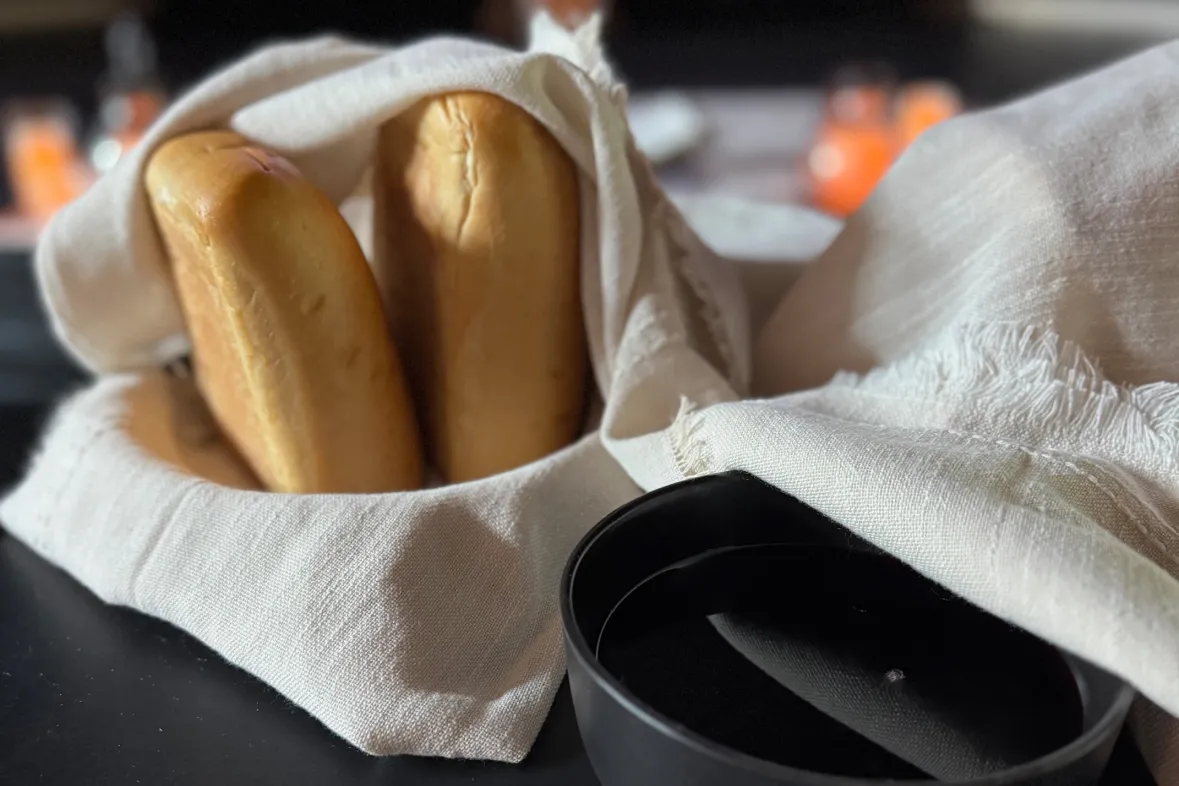 communion-1 Three bread rolls wrapped in a white cloth napkin next to a black dish on a table.