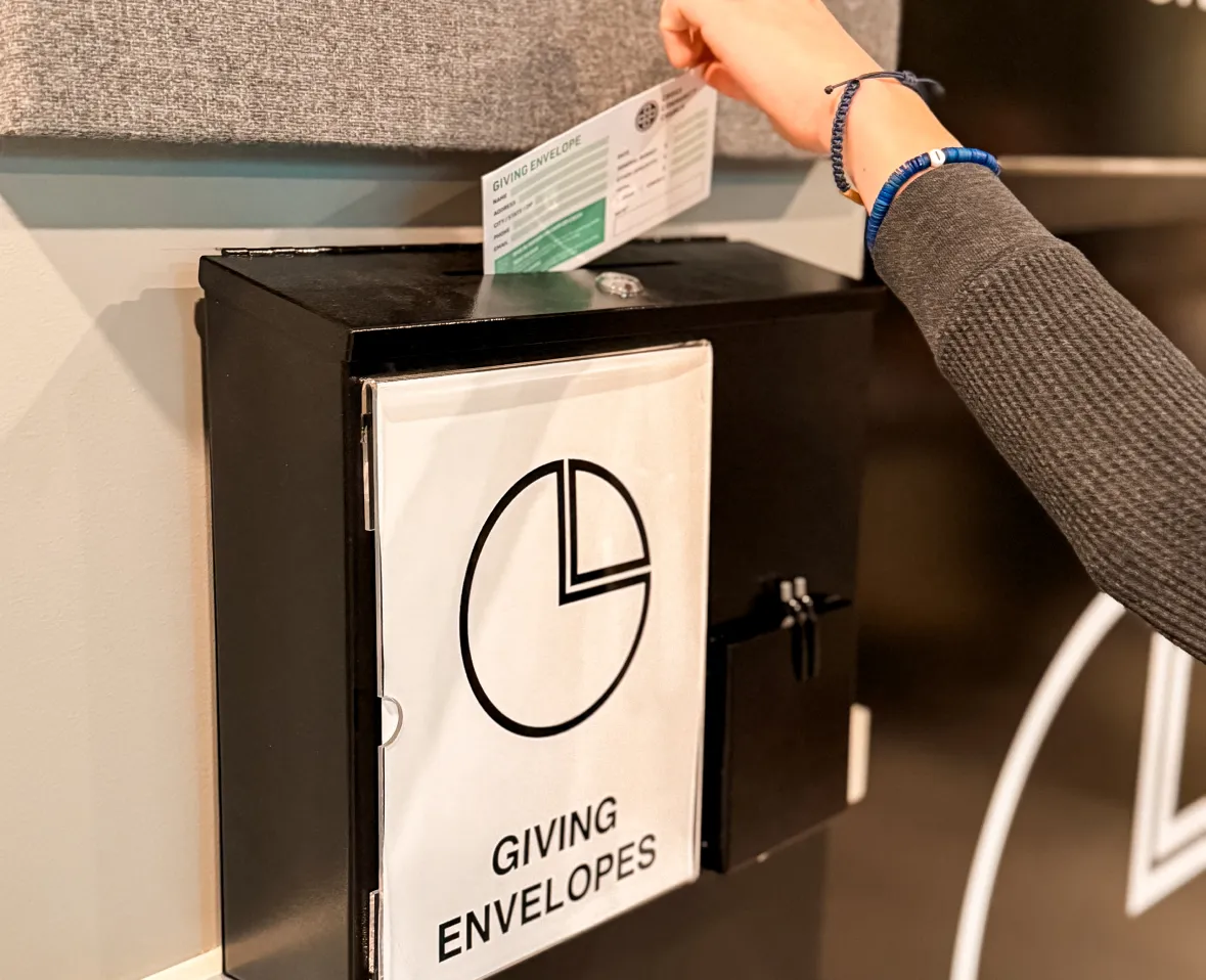 giving-img A person places a giving envelope into a black donation box labeled "GIVING ENVELOPES.